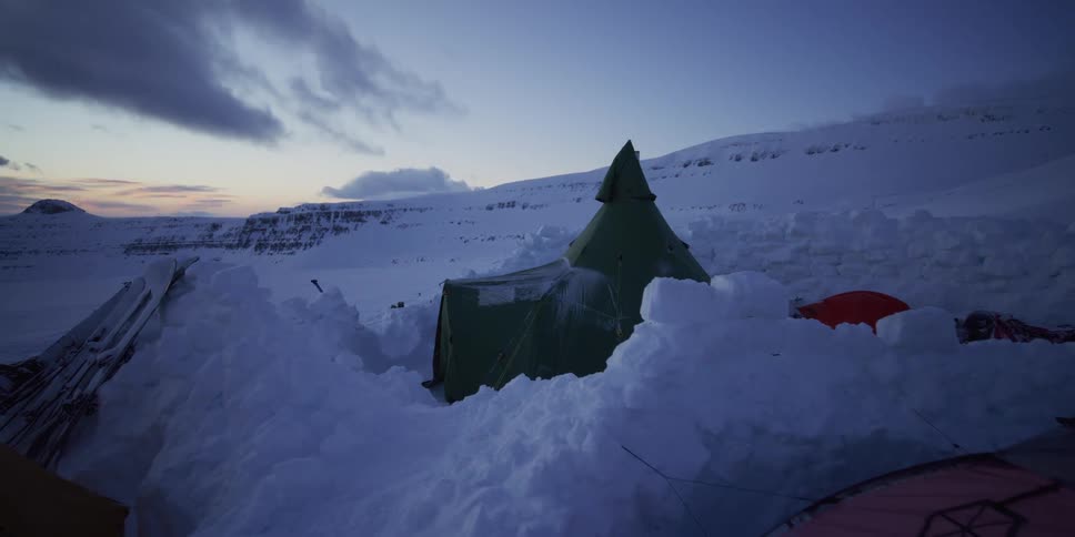 A remote arctic campsite with tents nestled in deep snow under the dim light of dusk
