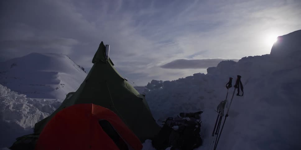 A remote winter campsite with a hot tent pitched on a vast snowy glacier in the mountains