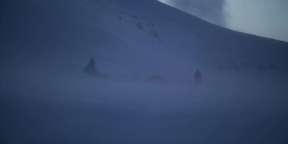 A mountain base camp with tents and a climber is slowly revealed through the blowing snow of a blizzard