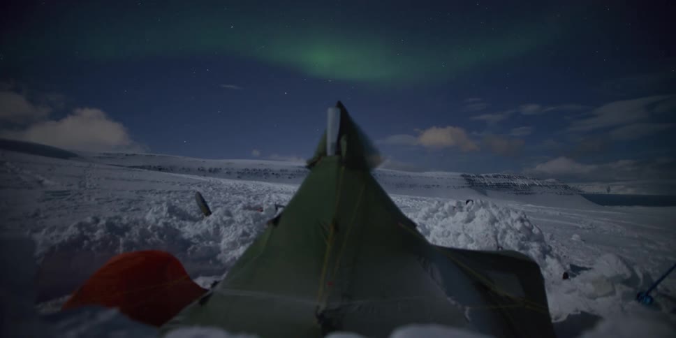 Timelapse of the Northern Lights dancing in the starry night sky over a campsite in the snowy mountains