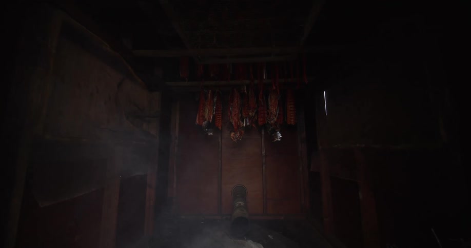 A slow push into a rustic wooden smokehouse reveals salmon fillets smoking over a smoldering fire