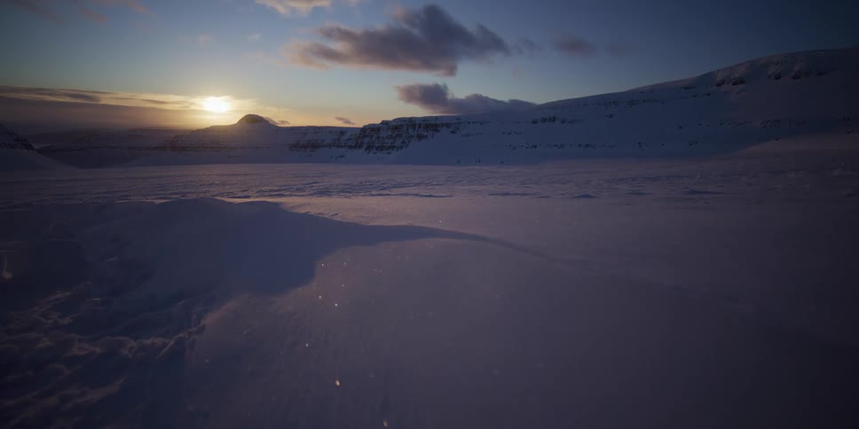 A slow dolly shot reveals a vast, pristine, snow-covered landscape sparkling under the golden light of a setting sun