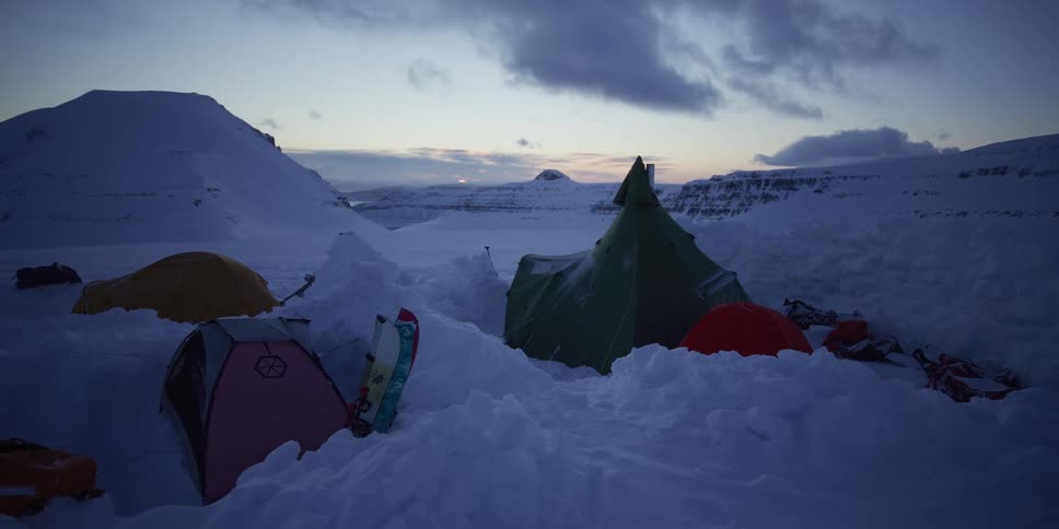 A remote expedition campsite with colorful tents pitched deep in the snow of a vast arctic valley at twilight
