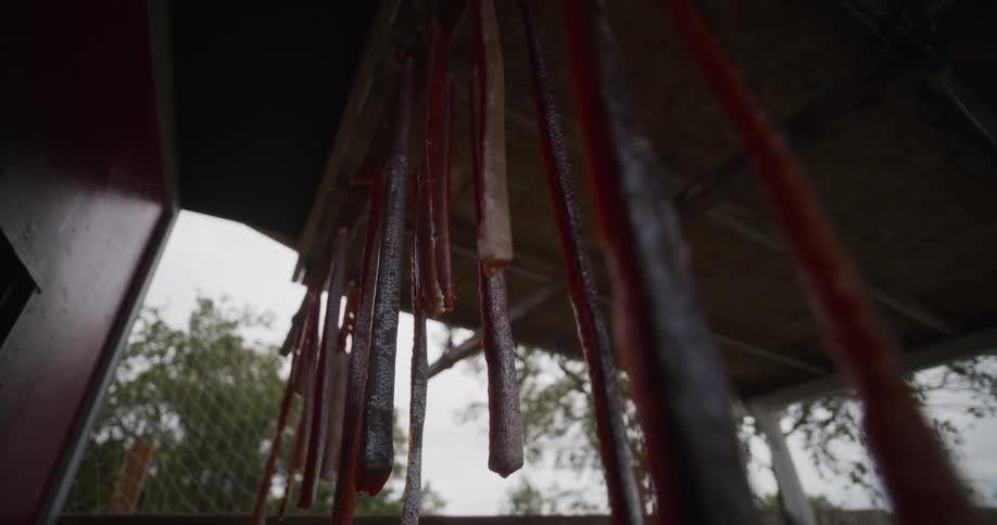 Low-angle shot of fresh salmon fillets hanging from a wooden rack to dry outdoors in a traditional preservation method