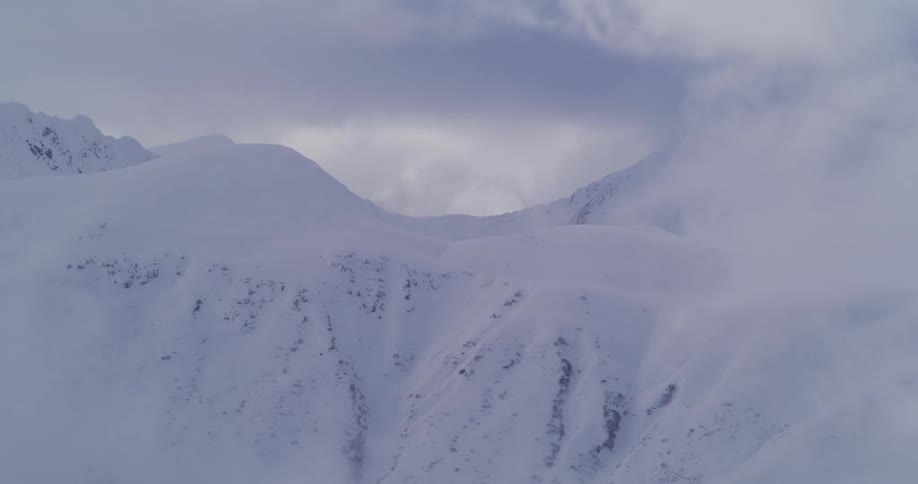 A static wide shot shows a vast, snowy mountain range as thick fog and clouds slowly drift across the peaks