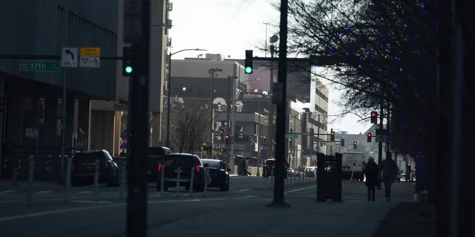 Cars wait at a green light on a sunny day on a downtown city street as people walk on the sidewalk