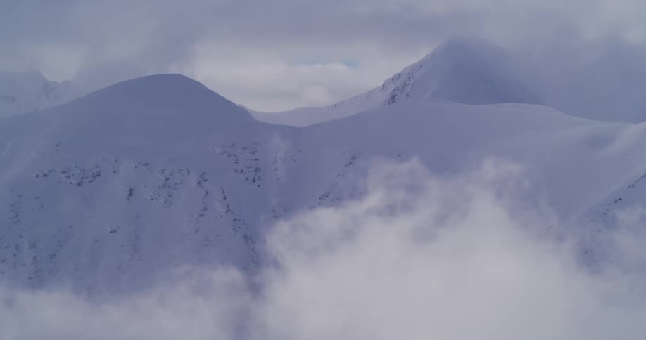 Majestic snow-covered mountains poke through a sea of swirling clouds and fog on a cold winter day
