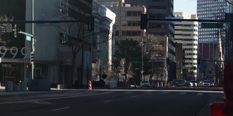 Cars drive through a downtown city street intersection surrounded by tall buildings in the bright sun