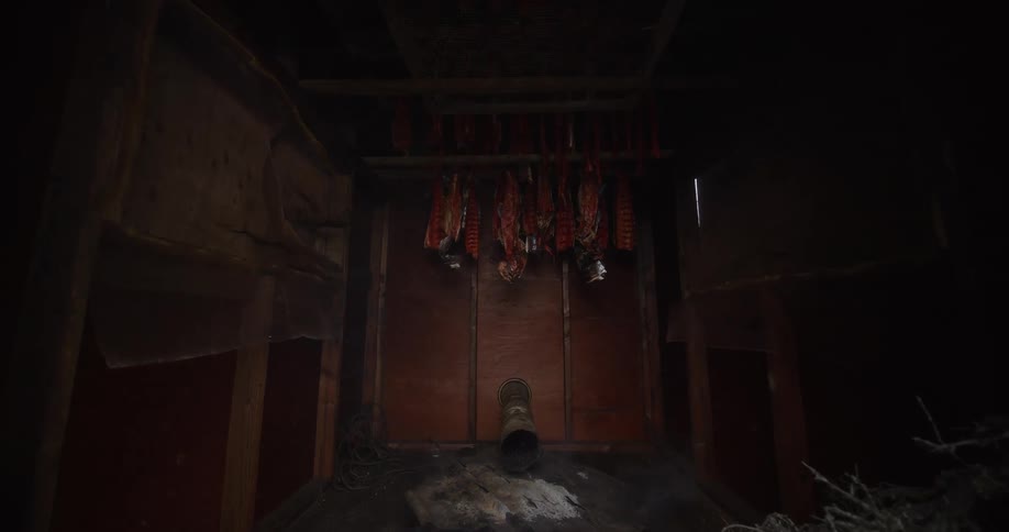 A slow push-in shot reveals salmon fillets hanging to smoke inside a dark and rustic wooden smokehouse