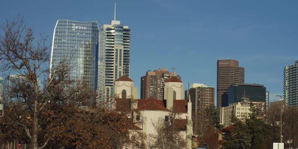 A static view of the modern Denver, Colorado skyline with a historic church in the foreground, as a car passes by on a clear day
