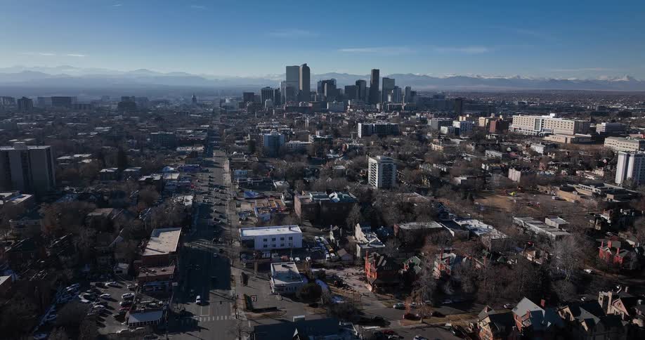 An aerial view of the Denver, Colorado skyline with the snow-capped Rocky Mountains in the distance on a clear sunny day