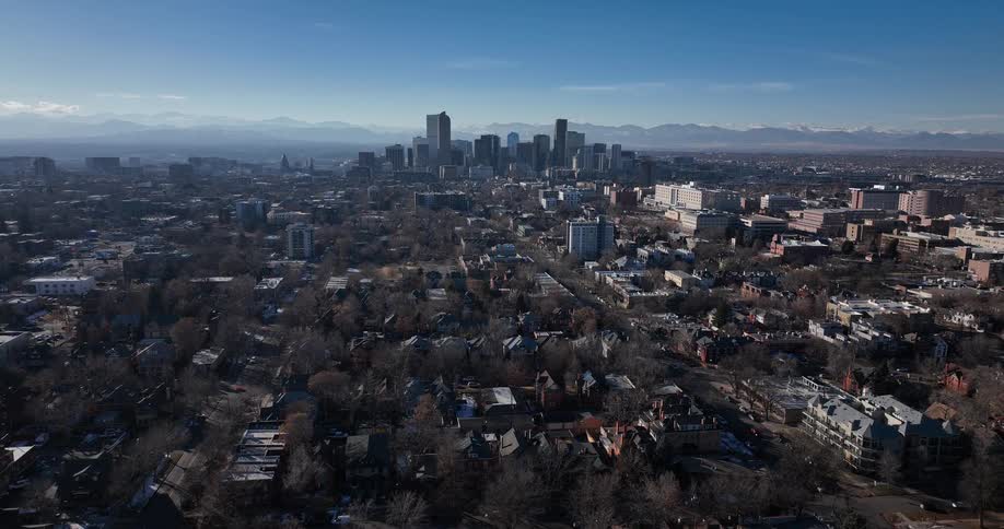 Slowly rising aerial view reveals the downtown Denver, Colorado skyline with the snow-capped Rocky Mountains in the distance on a sunny winter day
