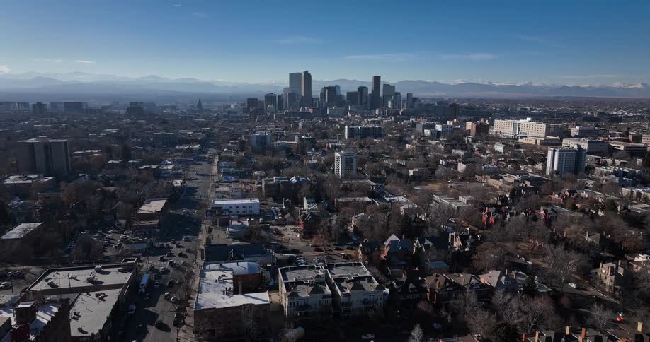 Slow aerial pullback shot of downtown Denver, Colorado, featuring the city skyline and the Rocky Mountains on a bright, sunny winter day