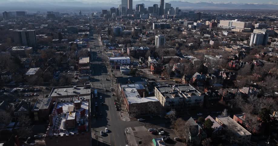 Aerial view of a city neighborhood, slowly tilting up to reveal the downtown Denver skyline and the distant Rocky Mountains