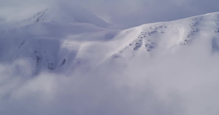 Aerial view of a majestic snow-covered mountain range shrouded in dense fog and clouds