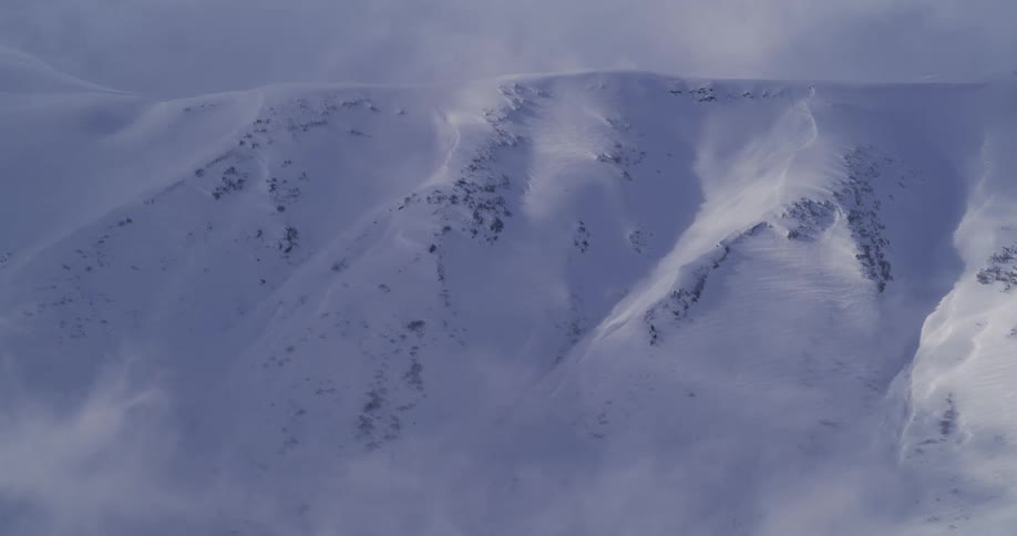 A harsh blizzard blows snow across a desolate, frozen mountain landscape