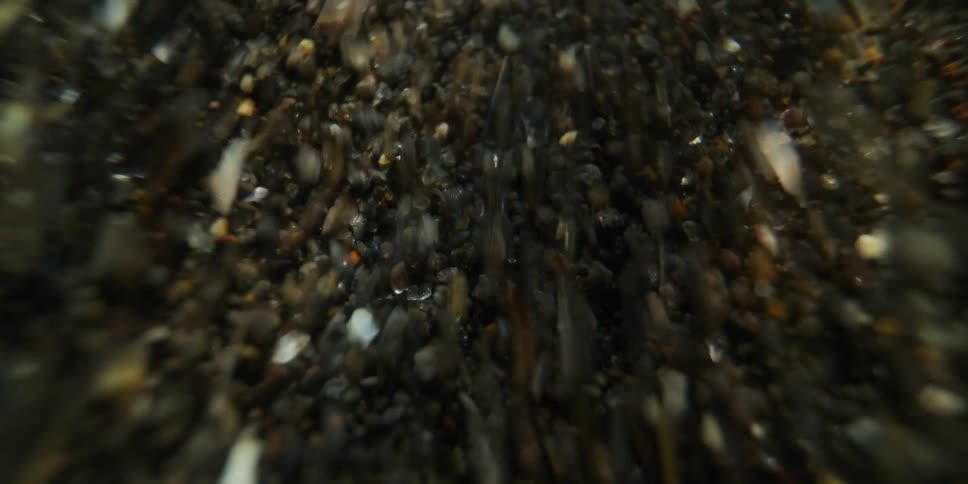 An extreme close-up, abstract view of sand and pebbles tumbling and swirling chaotically