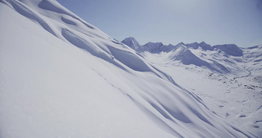 A lone skier carves down a massive, pristine powder slope in a stunningly beautiful mountain valley on a bright, sunny day