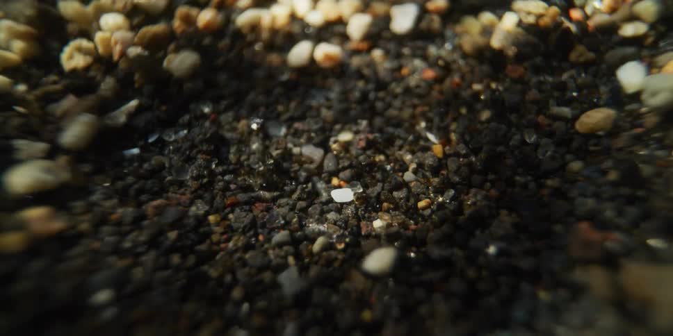 An extreme close-up, macro shot shows grains of sand and small pebbles bouncing and dancing from intense vibrations