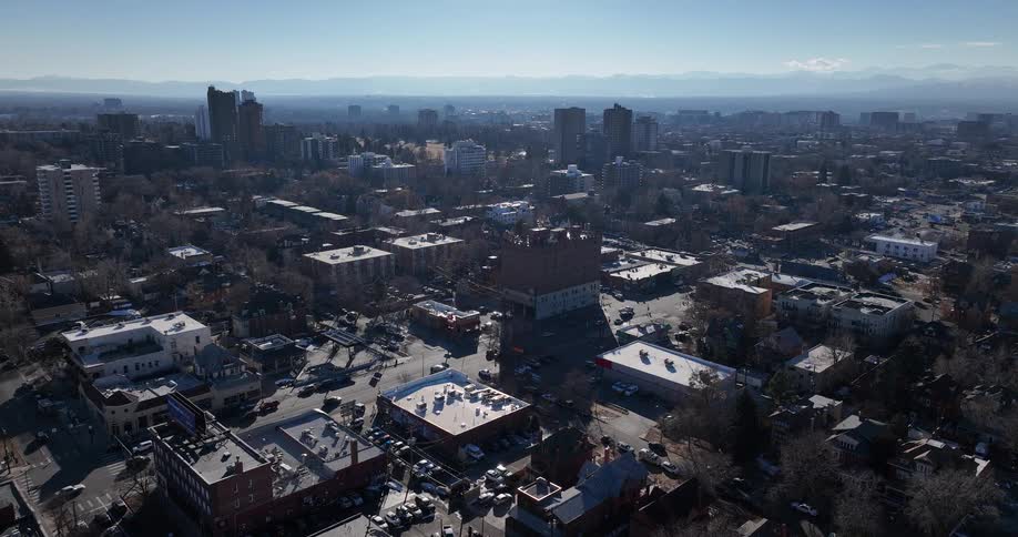 A wide aerial perspective shows a sprawling cityscape with active streets and mountains in the background under a clear sky
