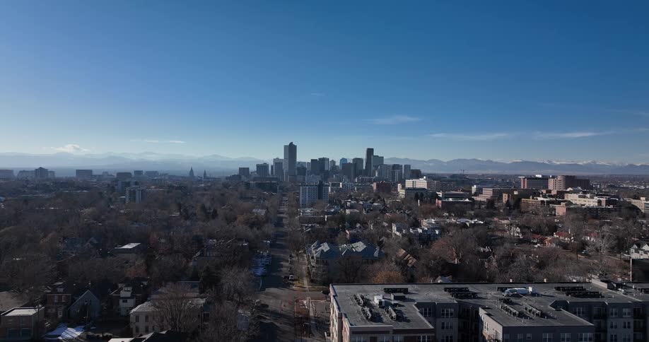 A slow, rising aerial view reveals the downtown Denver skyline and the majestic Rocky Mountains on a beautiful, clear day