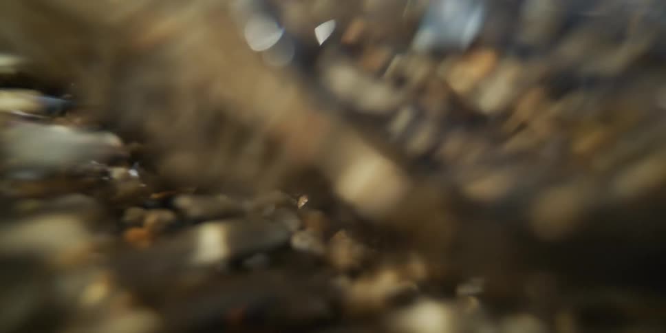 A dynamic macro shot shows swirling sand and shimmering water ripples over a pebble beach