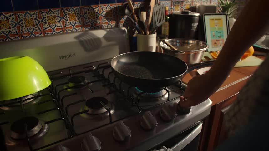 Slow motion shot of a person's hand turning a knob to ignite a gas stove burner under a frying pan in a kitchen
