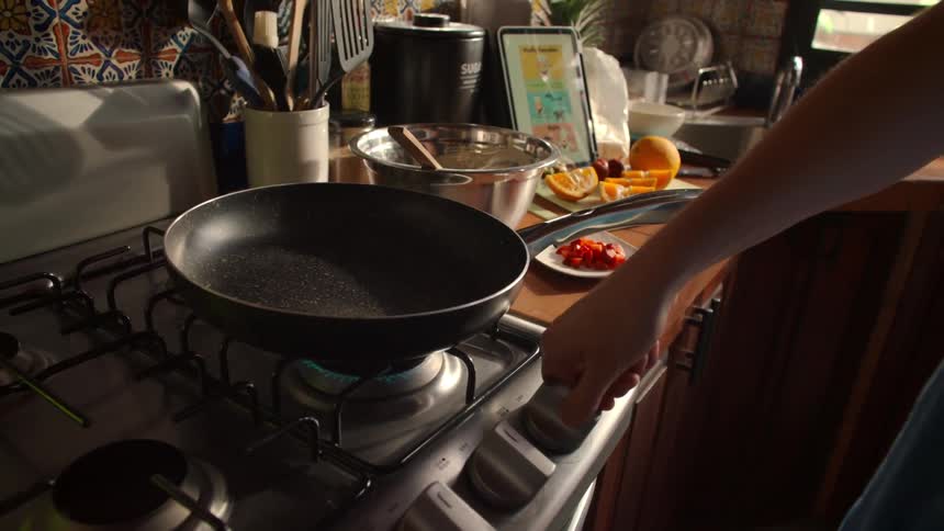 A person ignites a gas stove burner and checks the heat of a frying pan in slow motion before starting to cook