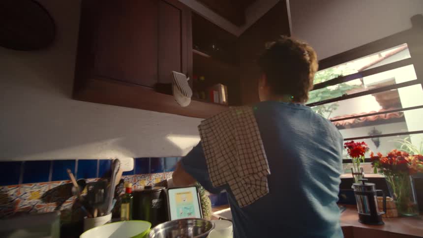 A man follows a recipe on his tablet to prepare breakfast in a rustic, sunlit kitchen