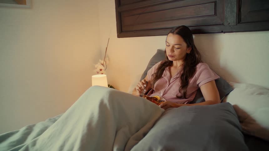A relaxed woman in pink pajamas enjoys eating a healthy meal from a bowl while sitting up in her cozy bed