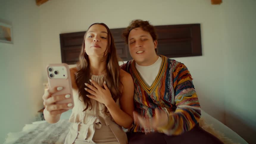 A happy young couple waves and smiles while on a video call using a smartphone in their cozy bedroom