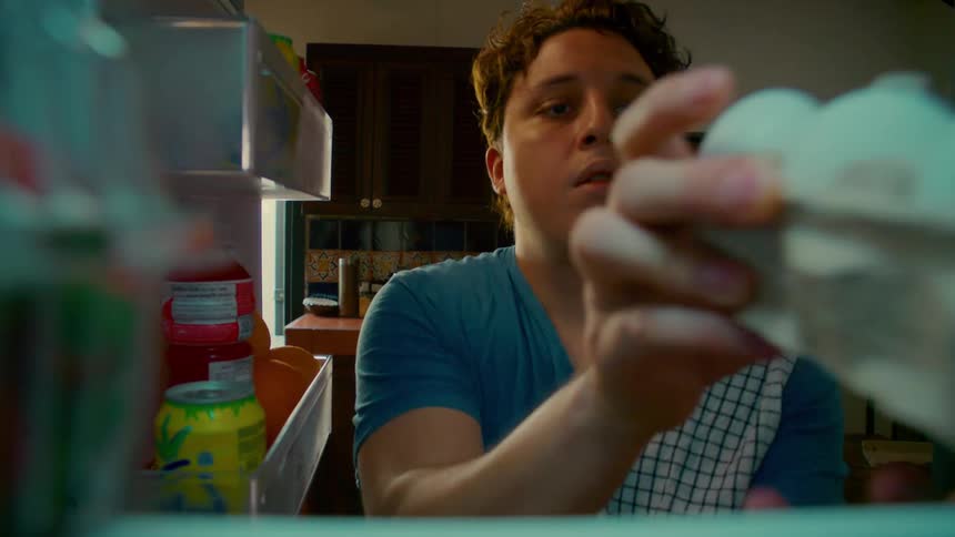 A young man opens a refrigerator in his kitchen and takes out a carton of eggs, shot from inside the fridge