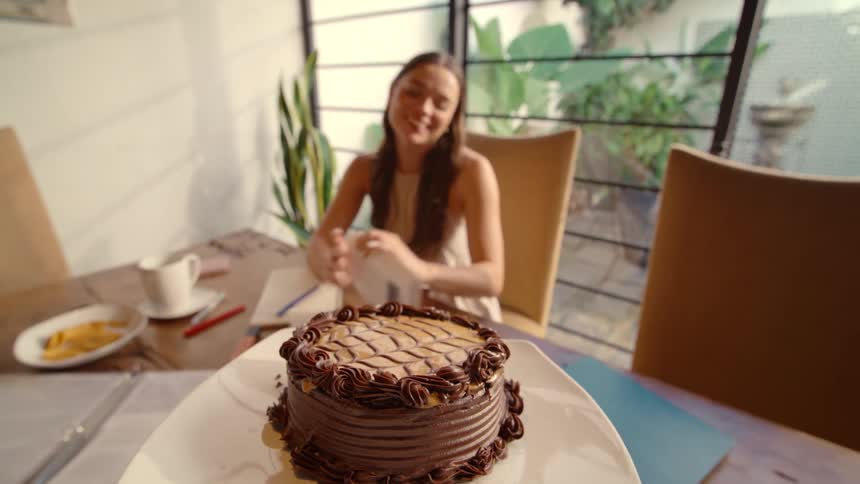 First-person point of view of surprising a happy young woman with a delicious chocolate cake while she studies at home