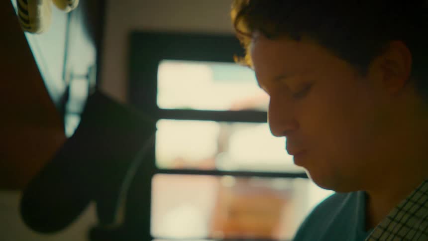A man in a sunlit kitchen prepares fresh strawberries and savors one with his eyes closed in slow motion
