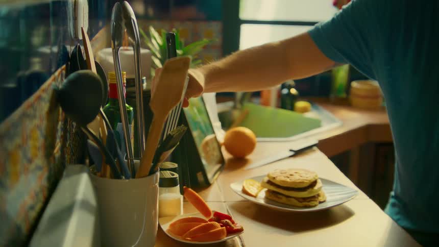 Man carefully plates a delicious breakfast of pancakes and fresh fruit in a warm, sunlit kitchen
