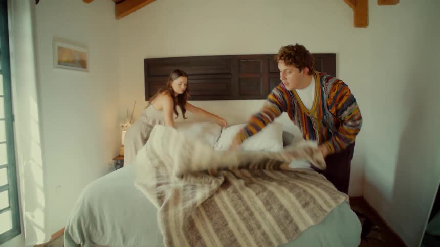 A happy young couple works together to make their bed in a bright and cozy bedroom