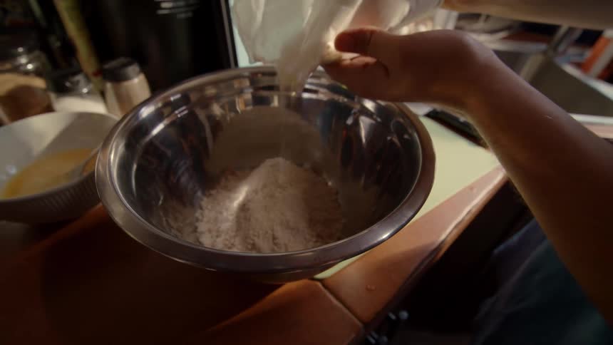 Following a cute pancake recipe on a tablet, a person pours flour into a steel bowl in slow motion