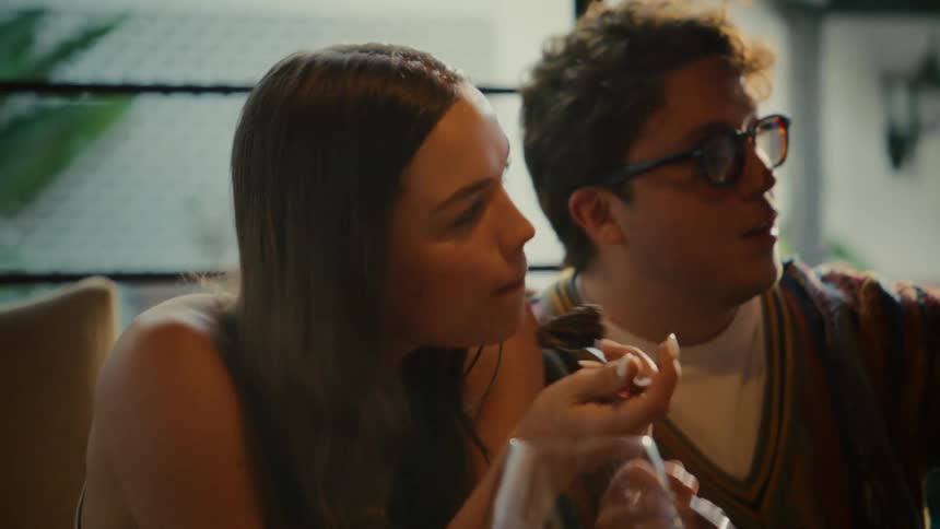 A smiling young couple on a date playfully feed each other chocolate dessert while taking a selfie at a restaurant