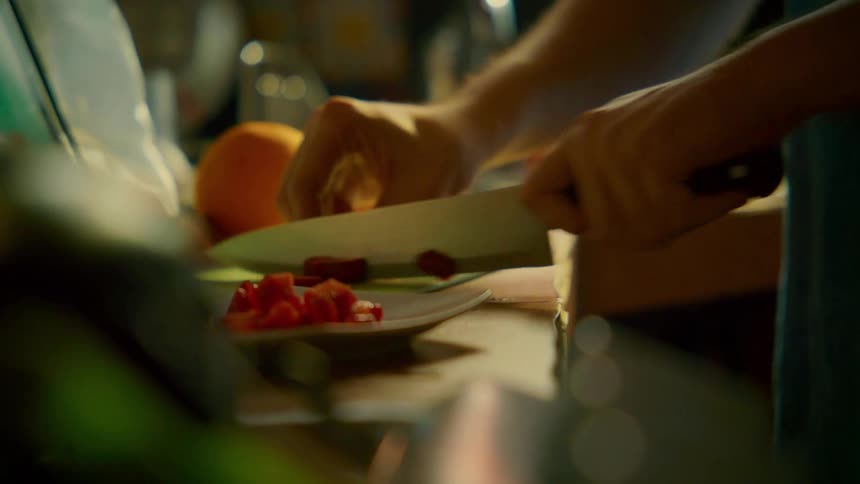 A close-up slow-motion shot of hands methodically slicing fresh strawberries and oranges on a cutting board in a warmly lit kitchen