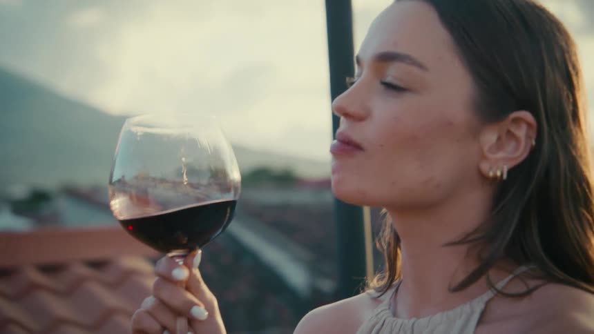 A young woman enjoys an intimate conversation and a glass of red wine with her date on a rooftop at sunset