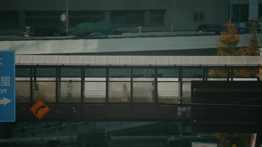 Pedestrians walk through a covered skywalk as traffic moves along multiple levels of a busy city highway