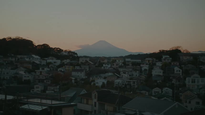 A timelapse view of Mount Fuji towering over a Japanese town at dusk
