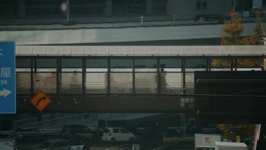 Silhouettes of people move across an enclosed pedestrian bridge above a bustling highway in Tokyo