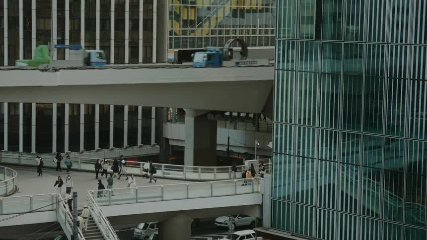 A high-angle, slow-motion view captures pedestrians on elevated walkways and traffic on highways amidst modern glass buildings in a bustling city