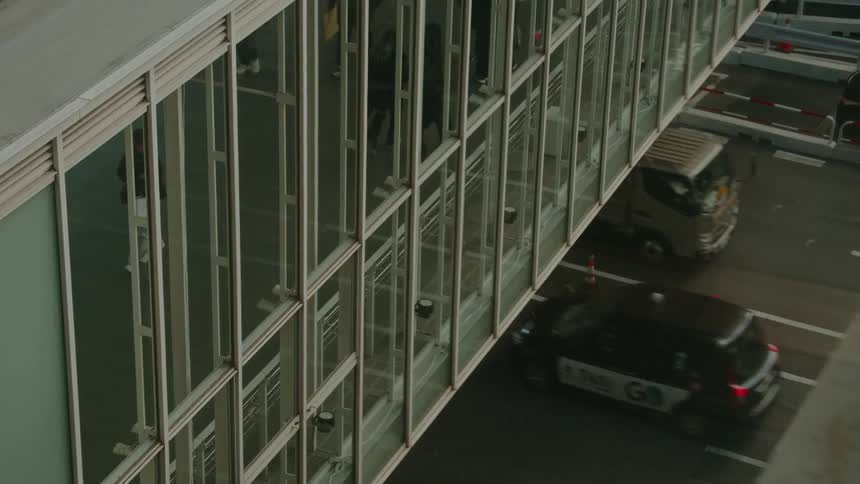 High-angle view of people walking through a glass skywalk as city traffic moves on the street below