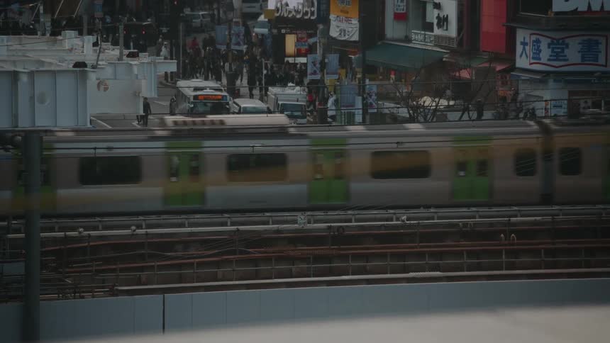 An elevated view shows a bustling Tokyo street with pedestrians crossing as multiple trains pass by on the tracks