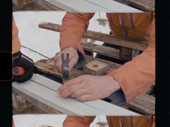 Vintage style footage of a worker's hands hammering a nail into a wooden plank in a snowy outdoor setting