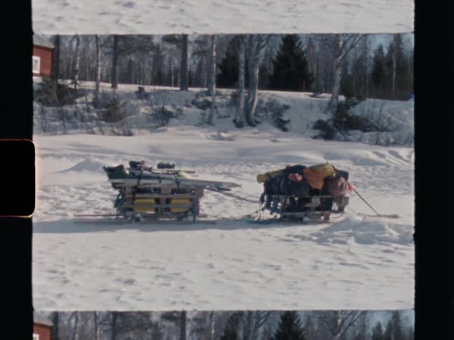 Vintage footage shows two pulk sleds loaded with gear and skis for a winter expedition