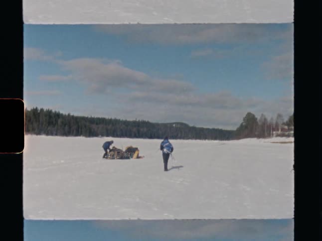 Archival footage of two people on a winter expedition, cross-country skiing across a vast frozen lake