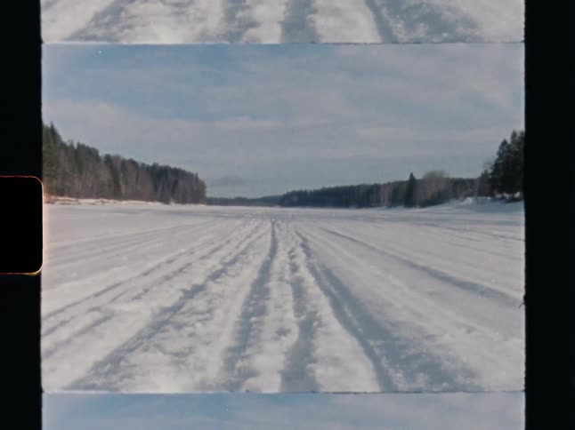 Vintage film shot of snowmobile tracks on a frozen river winding through a winter forest landscape
